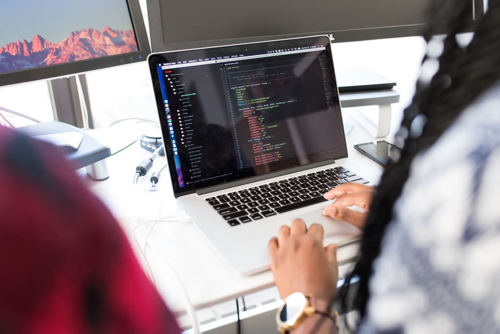 Close view of hands typing on a laptop displaying code, with a mountain landscape wallpaper on screen